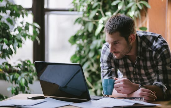 Young business man work on computer in his pleasant studio home office. Freelance professions in cool workplace environment: programmer, designer, architect, blogger, entrepreneur, social media. Natural light.