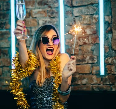 Young happy woman celebrating new year eve drinking champagne with fireworks. Lady clubber in nightclub having fun. Hipster girl at celebration luxury party.