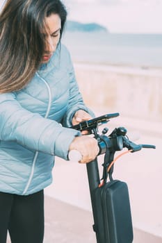 side view of Beautiful latin woman riding her motorized scooter in the city, activating smart phone app, mobility concept sustainable transport, zero CO2 emissions