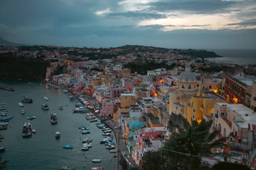 View of the Port of Corricella with lots of colorful houses after sunset in Procida Island, Italy.
