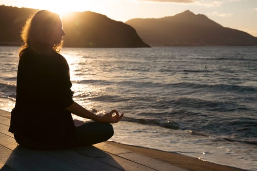 Woman in a yoga pose at sunset at the beach. Mindfulness and mental health concept.