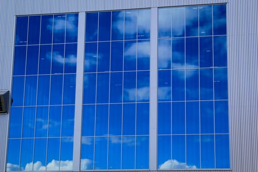 The blue sky and white clouds are reflected in huge windows.