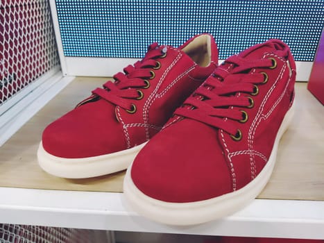 Red sneakers or sneakers made of natural suede on a store shelf. White flexible sole and red laces. Shoe shop. Youth comfortable fashionable shoes. Newest concept. The best red running shoes