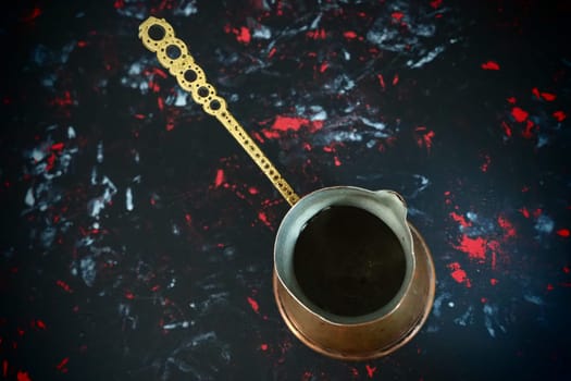 Balkan cezve for turkish coffee. A copper cezve on black surface. Antique bronze utensils. Carved metal handle with pattern. Black background with white, red and blue spots
