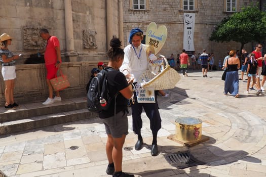 On the streets of Dubrovnik Croatia, happy vacationers walk and buy souvenirs from the seller in the national festive Croatian costume on August 15, 2022. Tourism industry. Summer day. Sale of goods.