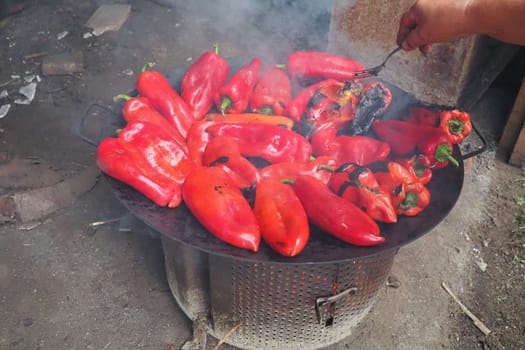 Roasting red peppers for a smoky flavor and quick peeling. Thermal processing of the pepper crop on metal circle. Brazier container used to burn charcoal fuel for cooking, heating or cultural rituals