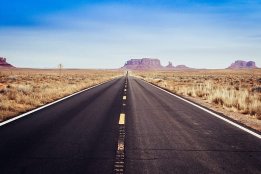 Lonely and deserted american road into the desert of monument valley with no cars, displaying vanishing point.