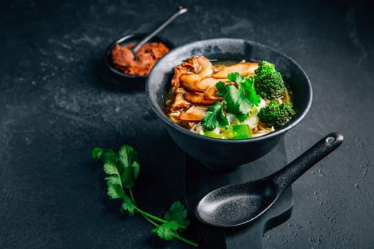 Vegan miso or ramen soup with mushrooms and vegetables on black background