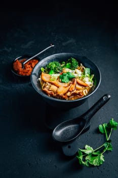 Vegan miso or ramen soup with mushrooms and vegetables on black background