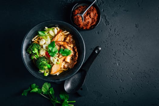 Vegan miso or ramen soup with mushrooms and vegetables on black background
