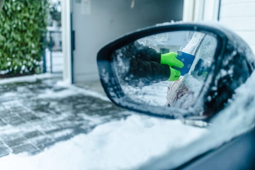 Teenager cleans car after a snowfall, removing snow and scraping ice