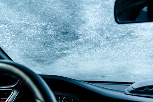 Frozen car windshield covered with ice and snow on a winter day. Selective focus.