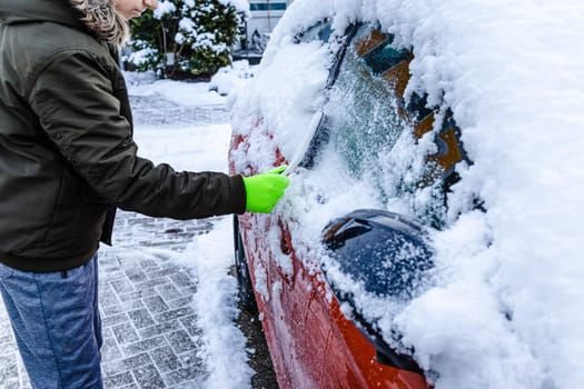 Teenager cleans car after a snowfall, removing snow and scraping ice