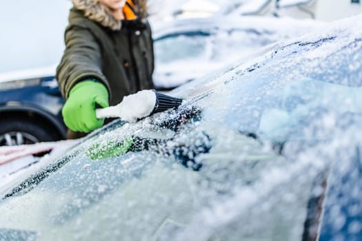 Teenager cleans car after a snowfall, removing snow and scraping ice