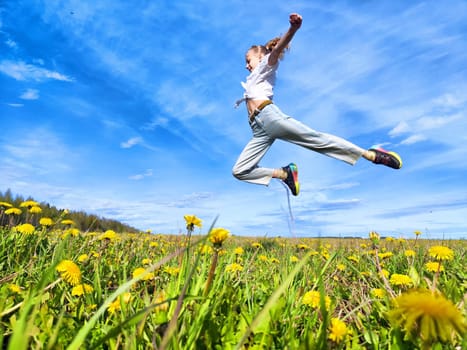 A person expresses happiness by jumping in a lush field of dandelions, surrounded by a clear blue sky on a sunny day.