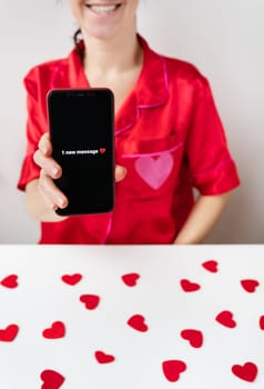 A happy girl is holding a smartphone with an activated screen with 1 SMS message in the shape of a heart. Concept of Valentine's Day, February 14