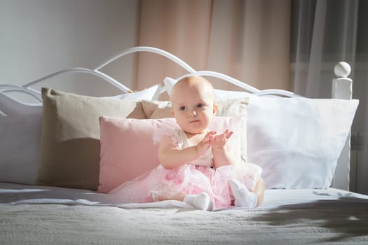 A baby in a pink tutu crawls on a bed surrounded by soft pillows, exploring the cozy space.