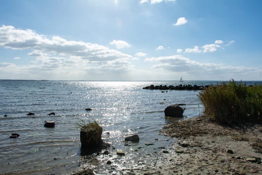 Breakwater made of large stones in the water on the Baltic Sea coast, sailing ship on the horizon, with grass on the beach on the island of Poel, Germany, Europe