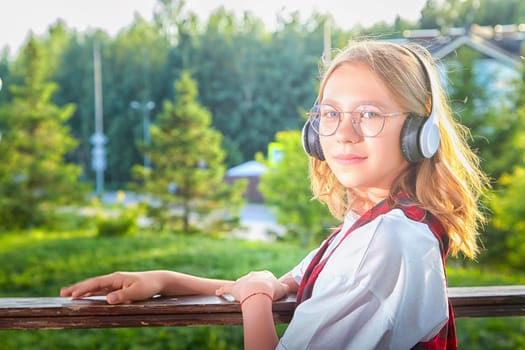 A girl wearing headphones leans against a wooden railing, surrounded by lush greenery in a tranquil outdoor setting.