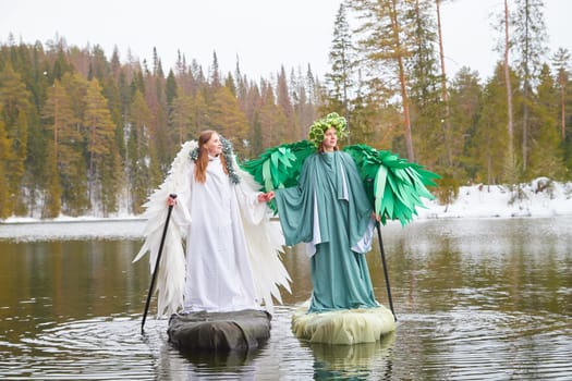 Two girls dressed in contrasting white and green outfits embody the essence of winter and spring beside a tranquil lake, capturing seasonal change.