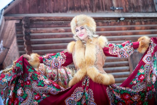 A Russian girl in a vibrant national dress poses with a horse during the Maslenitsa holiday festivities in winter.
