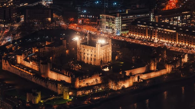 Aerial view of illuminated London tower, orange yellow street lights starting glowing to streets.