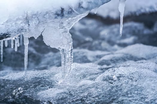 Ice on frozen river, closeup detail, water flows over rocks forming waves and bubbles - winter background.