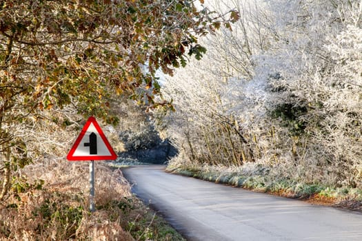 Frozen winter rural road with triangle warning sign and lined with beautiful frosty trees.