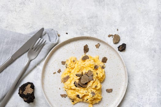 Scrambled eggs with sliced fresh black truffles from Italy served in a plate near fork and knife top view. Italian cousine, gourmet breakfast