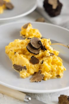 Scrambled eggs with sliced fresh black truffles from Italy served in a plate close up. Italian cousine, gourmet breakfast