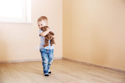Cute boy sitting standing in empty room. Concept of family relocation, rental apartment and home ownership.