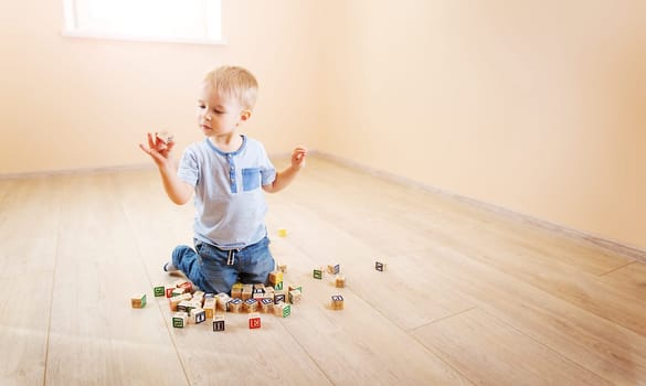 Little boy sitting on the floor indoor and playing with wooden cubes. Concept of preschool and kindergarten.