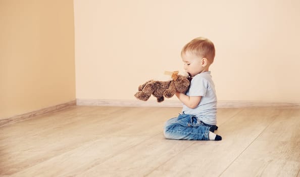 Cute boy sitting on the floor indoor. Concept of family relocation, rental apartment and home ownership.