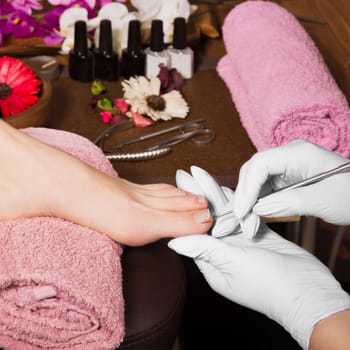 Closeup finger nail care by pedicure specialist in beauty salon. Pedicurist clear cuticle professional scissors for manicure and pedicure.