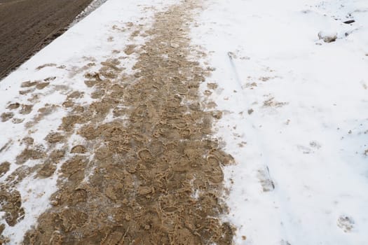 Many footprints of shoes and boots on the snowy pavement. Winter in the city. Wet weather and freezing temperatures. Weather forecast. Ice, white snow and muddy tracks with clay on the road