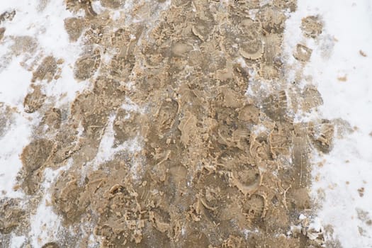 Many footprints of shoes and boots on the snowy pavement. Winter in the city. Wet weather and freezing temperatures. Weather forecast. Ice, white snow and muddy tracks with clay on the road