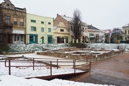 Sremska Mitrovica Serbia 01.27.2023 Snowfall in the city. Zhitni trg historical square. Ancient multi-colored buildings and excavations of Roman times. Weather forecast. Day winter. Cultural heritage