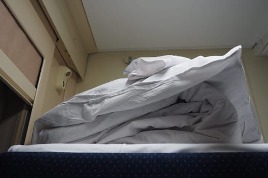 A set of bed linen on the top shelf of a railway car compartment. A bed made by a conductor. Night train ride. Pillow in a clean pillowcase. A folded blanket in a duvet cover. New coupe after repair
