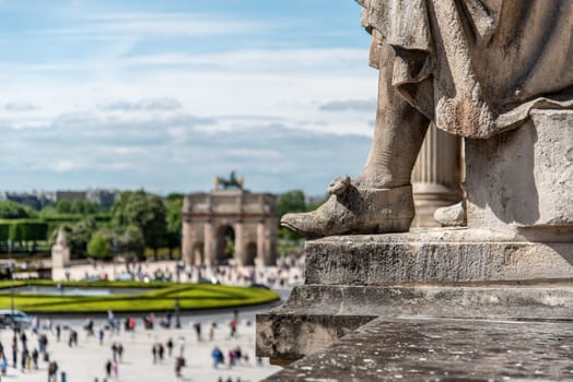 The foot of a statue on the roof of Louvre Palace with a triumphal arch in the background, Paris, France