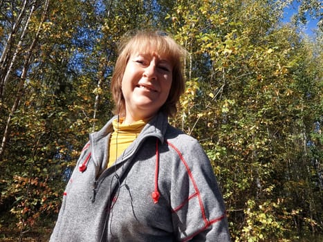 Blonde woman takes a cheerful selfie during her nature trip, surrounded by vibrant autumn foliage and trees.