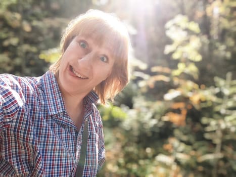 A blonde woman makes funny faces while taking a selfie on her journey through a vibrant forest.