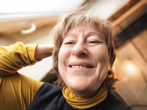 A blonde middle-aged woman takes a cheerful selfie, capturing her joyful moment during her latest travel experience.