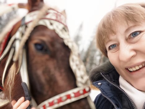 Blonde woman takes a joyful selfie with a horse, capturing a memorable moment on her winter journey.