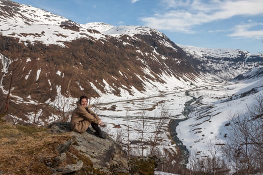 Mountains, snow-covered fjord, Girl sitting on the background of the valley. Norway in the spring