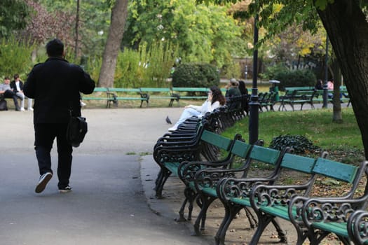 October 12, 2022 Bucharest, Romania, Europe travel , business man walking, street capital city, green recreation park benches people coming autumn landscape vacation walk, wooden tourists nature