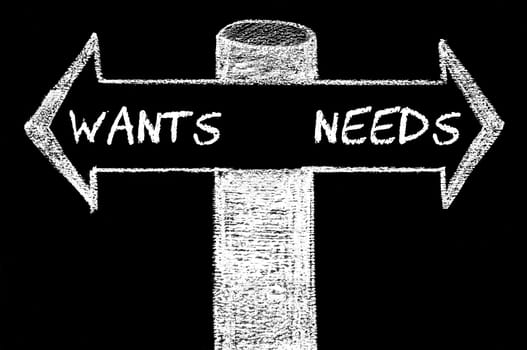 Opposite arrows with Wants versus Needs. Hand drawing with chalk on blackboard. Choice conceptual image