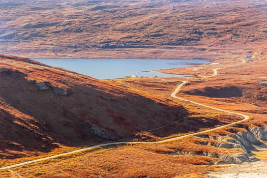 Autumn greenlandic orange tundra landscape with road to the lake and mountains in the background, Kangerlussuaq, Greenland