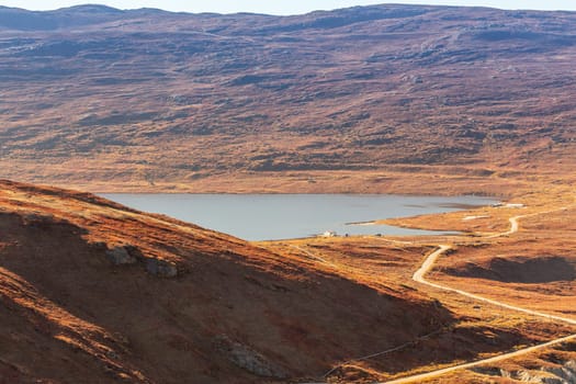 Autumn greenlandic orange tundra landscape with road to the lake and mountains in the background, Kangerlussuaq, Greenland