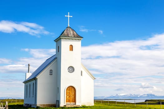 Flateyjarkirkja white lutheran church with meadow in foreground and sea  fjord with blue sky and mountains in the background, Flatey island, Iceland