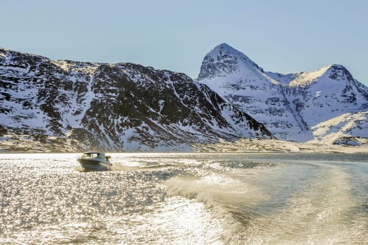 Motor boat in the middle of Nuuk fjord with frozen rocks in the background, Greenland